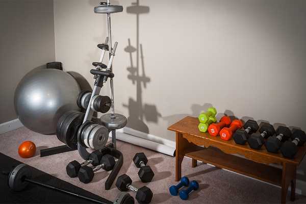 Multiple sets of dumbells and an exercise ball kept in the corner of a home gym.